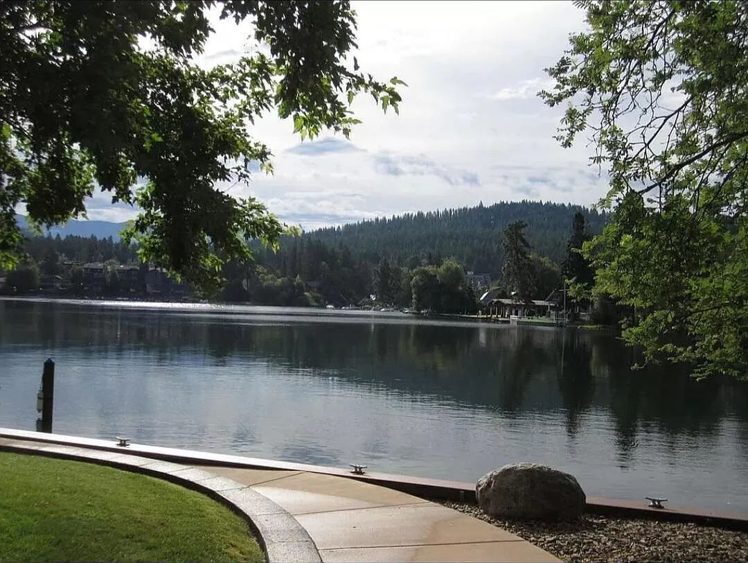 A tranquil lakeside view with a clear sky, a wooden dock, and a stone pathway leading to the water.