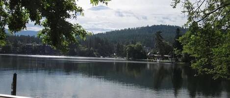 A tranquil lakeside view with a clear sky, a wooden dock, and a stone pathway leading to the water.