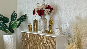 Una sala de estar moderna con una pared blanca de diseño geométrico, un mueble blanco y dorado y una alfombra color beige.