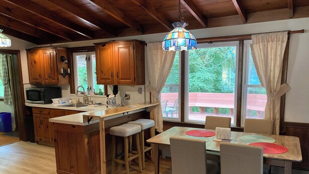 A wooden kitchen with a central island, bar stools, and a dining table with chairs. - Cozy Home in Pownal VT (Pownal)