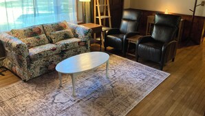 A living room with a floral sofa, a black leather chair, a small table, and a patterned rug. - Cozy Home in Pownal VT (Pownal)