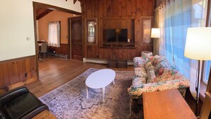 A cozy living room with wooden walls, a floral sofa, a white table, and a patterned rug. - Cozy Home in Pownal VT (Pownal)