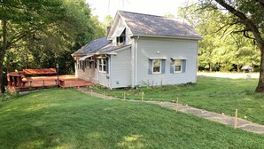 A small, single-story house with a porch, surrounded by a well-maintained lawn and trees. - Cozy Home in Pownal VT (Pownal)