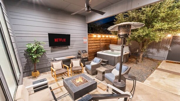 Un área exterior con una chimenea, asientos, una pantalla de televisión que muestra 'NETFLIX' y un calentador de patio.