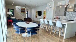 Una cocina moderna con una isla central, taburetes blancos y un comedor con una mesa redonda y sillas azules.