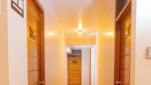 Un pasillo con puertas de madera, cada una marcada con un número. El piso está cubierto de baldosas y las paredes son blancas.