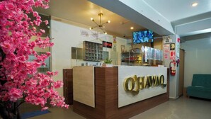 Un mostrador de recepción con un cartel que dice "O'Hawao" y un reloj digital que marca las 15:32.