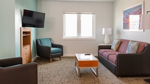 Una sala compacta con televisión, sofá, sillón, mesa de centro y ventana.