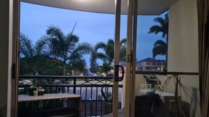 A balcony with wicker furniture, a potted plant, and a view of palm trees and a street. - Splashpark family resort, full of fun. Close to theme parks, beach, restaurants (Mermaid beach)