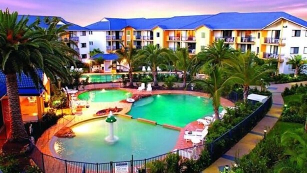 A hotel with a large outdoor swimming pool surrounded by palm trees and lounge chairs. - Splashpark family resort, full of fun. Close to theme parks, beach, restaurants (Mermaid beach)