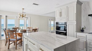 Una cocina moderna con encimeras de mármol, sillas de madera y vistas al océano.