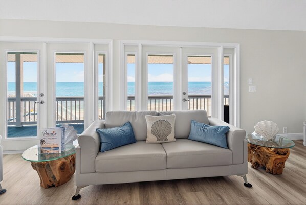 Un salón con un sofá color beige, dos almohadas azules, una mesa de centro de vidrio con base de madera y un libro de bienvenida.