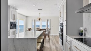 Una cocina moderna con una isla de mármol, taburetes de madera y vistas al océano.