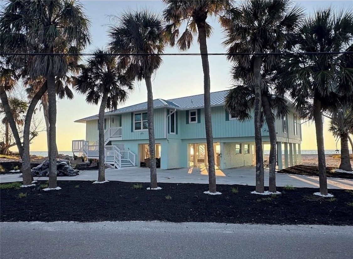 A light blue two-story house with a porch, surrounded by palm trees.
