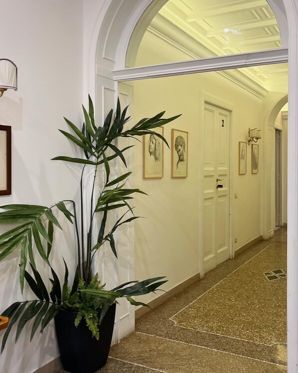 A hallway with a potted plant, framed portraits on the wall, and a door at the end. - Il Plancton Colosseo (Rome)