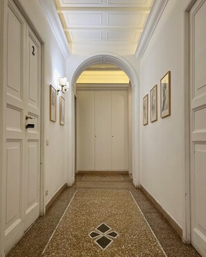 A hallway with white doors, framed artwork on the walls, and a patterned floor. - Il Plancton Colosseo (Rome)