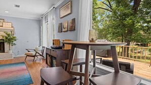 Un salon moderne avec une cheminée, un coin repas avec une table et des chaises, et une grande fenêtre donnant sur une terrasse et des arbres.