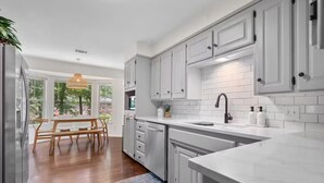 Une cuisine moderne avec des meubles blancs, un grand îlot central et un coin repas comprenant une table et des chaises en bois.
