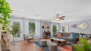 Un salon spacieux comprenant un canapé, des poufs, une table basse et un ventilateur de plafond.