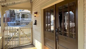 A wooden porch with a white picket fence, a wooden door with glass panels, and a stone staircase leading to a covered area. - Wishing Star Townhouse on Spring Street (Eureka Springs)