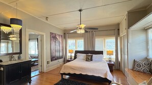 A bedroom with a bed, bedside lamps, a ceiling fan, a large mirror, and a dark rug. - Wishing Star Townhouse on Spring Street (Eureka Springs)