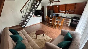 Una sala de estar con un sofá, una mesa de centro y una escalera que lleva a una zona de cocina.