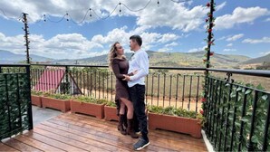 Una pareja en una terraza de madera con vistas a colinas y cielo despejado.