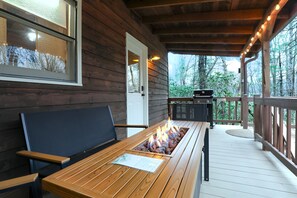 Een houten terras met een vuurkorf-tafel, zitplaatsen buiten en een barbecue.