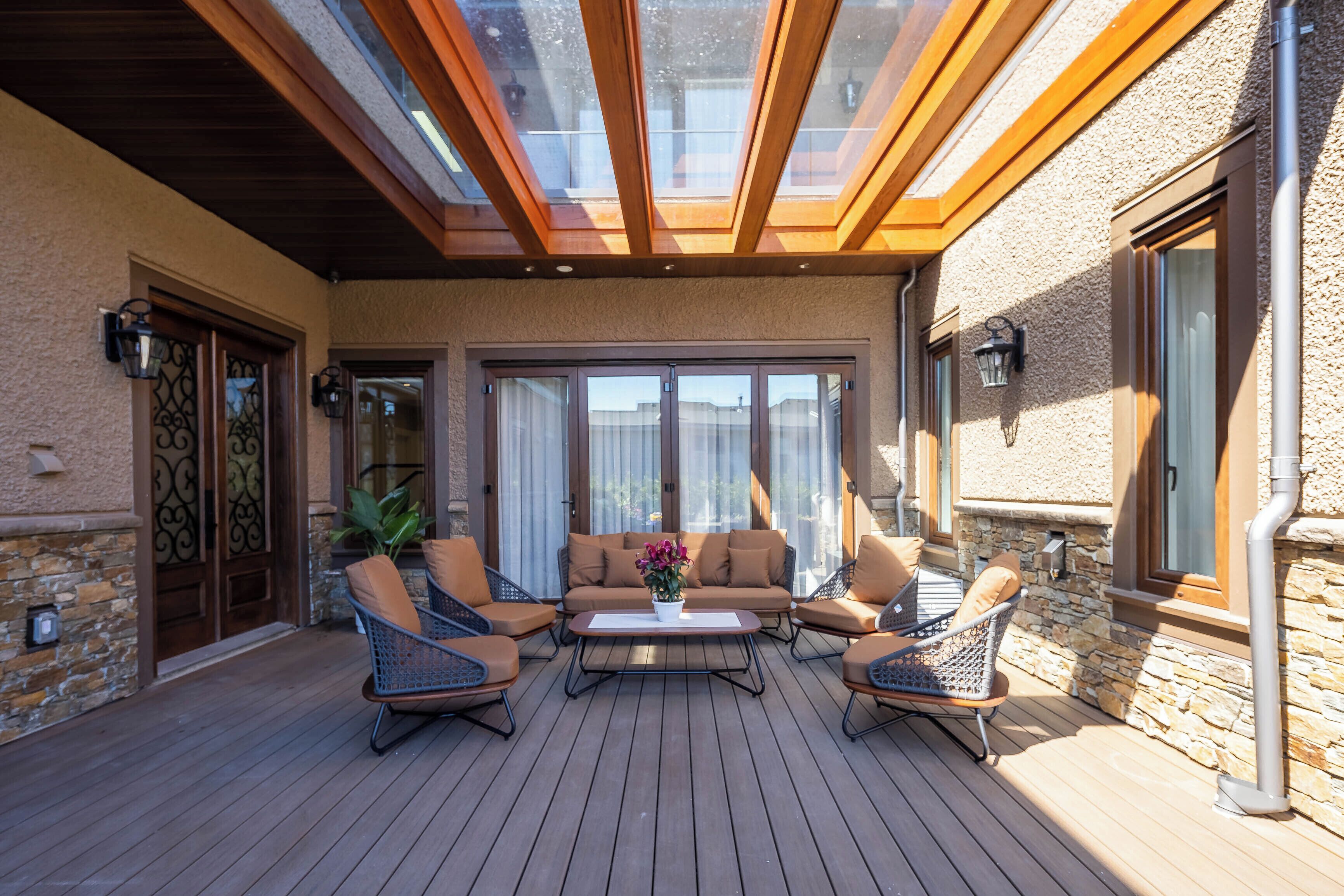 Eine überdachte Terrasse mit Holzboden, Gartenmöbeln und einem Oberlicht.