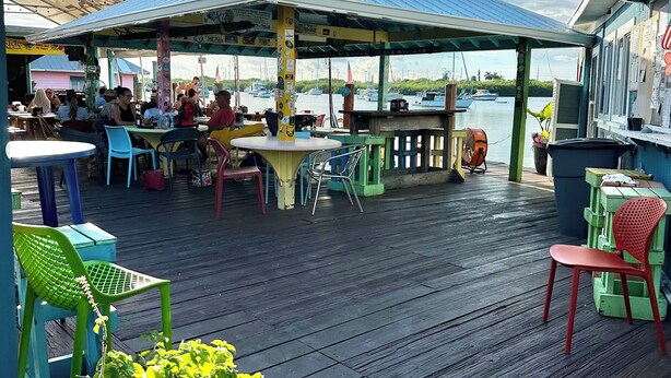 An outdoor seating area with tables and chairs, a covered section, and a view of boats on the water. -     Snowbird Paradise Canal-Front 1BR Minutes to Sombrero (Marathon)