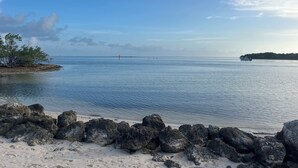 A beach with clear water, rocky shoreline, and a distant island. -     Snowbird Paradise Canal-Front 1BR Minutes to Sombrero (Marathon)