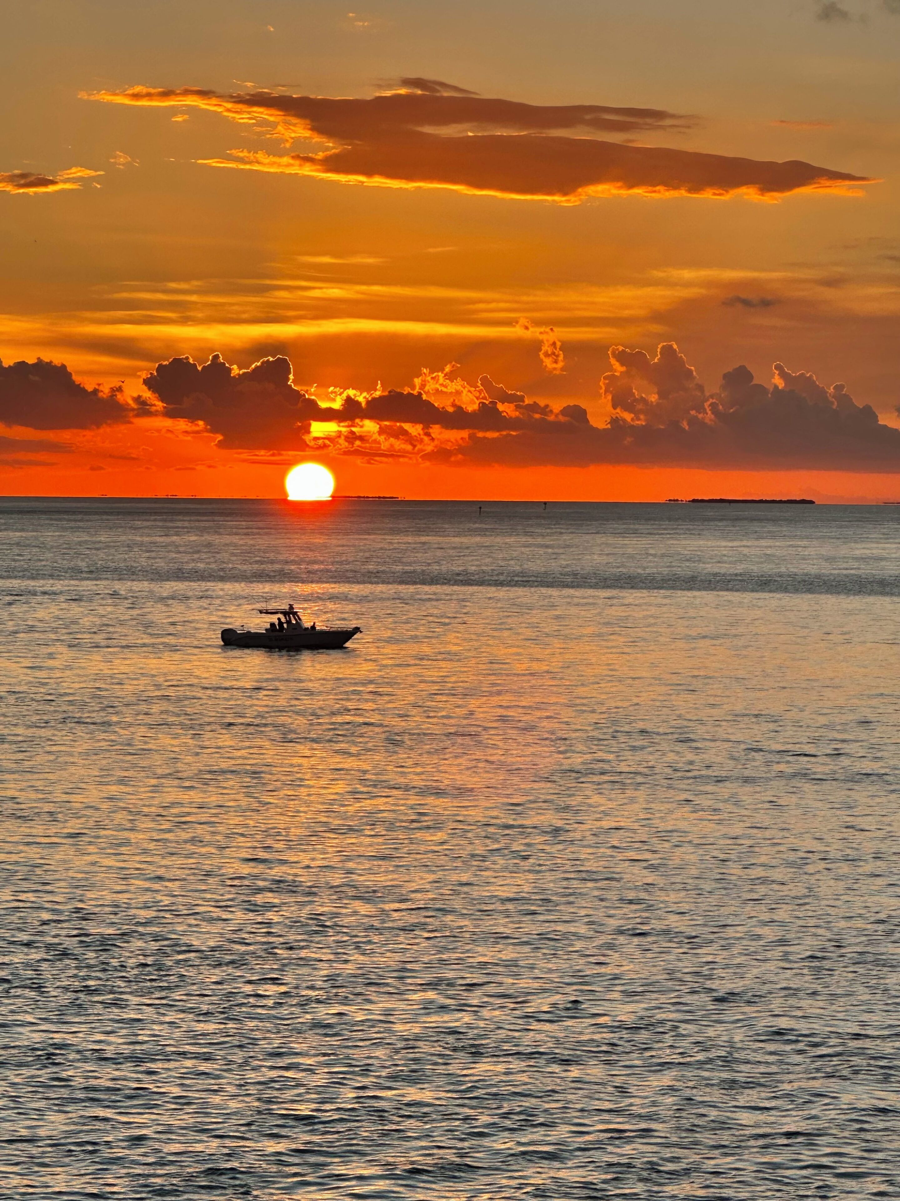 A sunset over a calm sea with a small boat in the distance.