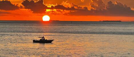 A sunset over a calm sea with a small boat in the distance.