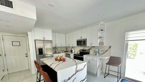 A modern kitchen with white cabinetry, a marble island, stainless steel appliances, and a view of the outdoors. -     Snowbird Paradise Canal-Front 1BR Minutes to Sombrero (Marathon)