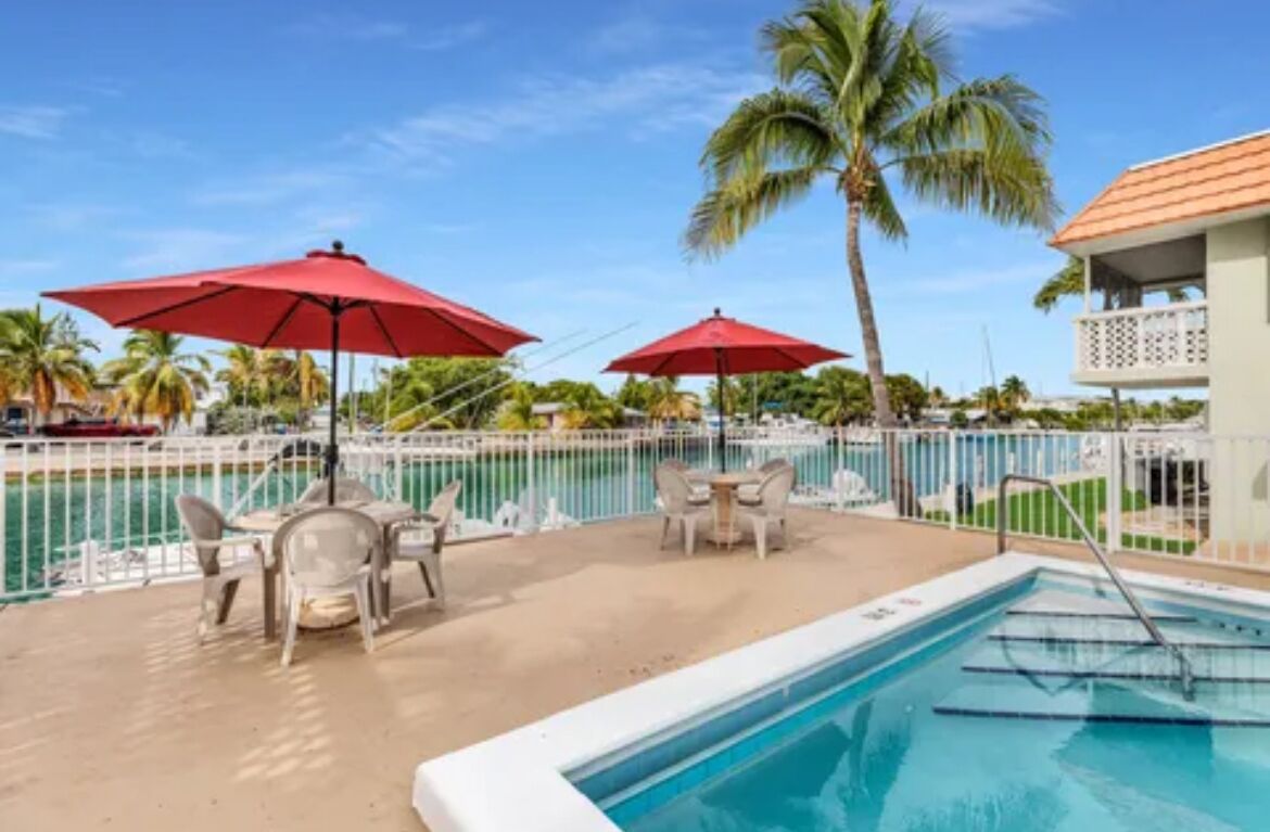 A poolside area with two red umbrellas, lounge chairs, and a pool.