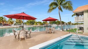 A poolside area with two red umbrellas, lounge chairs, and a pool. -     Snowbird Paradise Canal-Front 1BR Minutes to Sombrero (Marathon)
