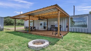 Un patio couvert équipé d’un barbecue et de sièges, d’un foyer extérieur et offrant une vue sur une serre.
