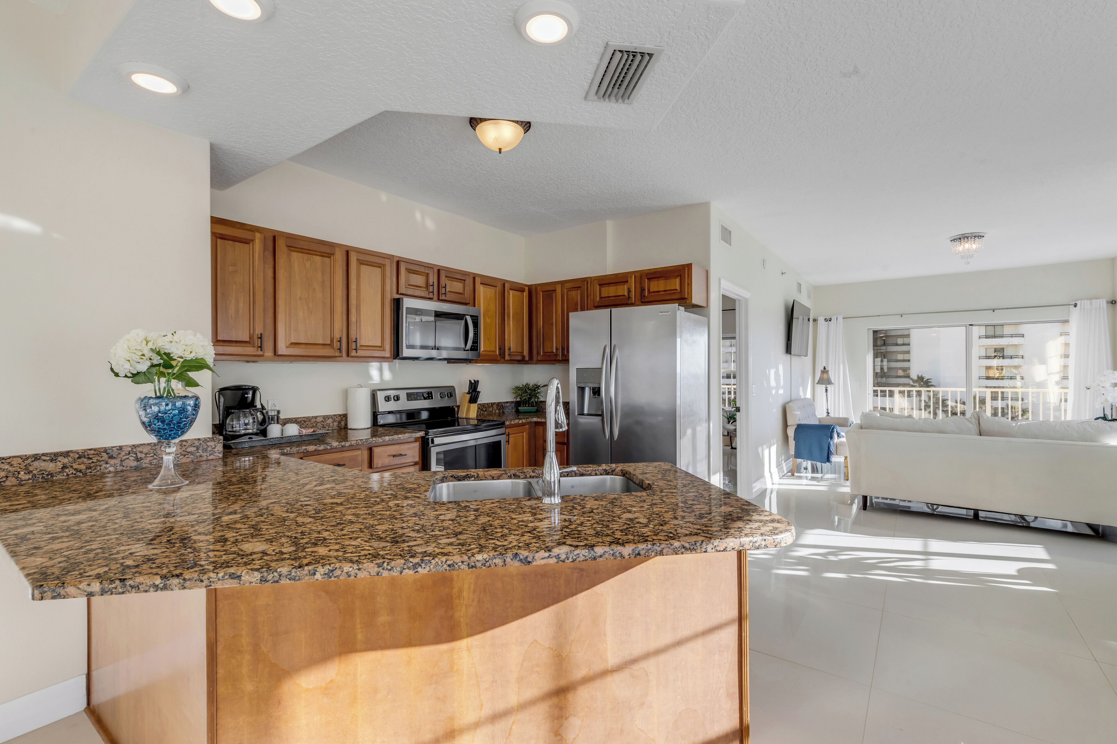A modern kitchen with granite countertops, wooden cabinets, stainless steel appliances, and a large island with a sink.