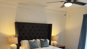 A bedroom with a large bed, two bedside tables, a ceiling fan, and a patterned rug.
