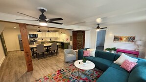 A spacious living room with a teal sofa, a colorful rug, and a dining area with a kitchen in the background.