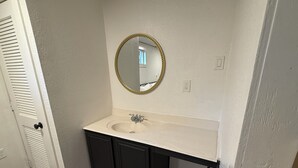 A bathroom with a white sink, dark cabinets, and a gold-framed mirror.