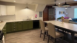 A modern kitchen with green cabinets, a white backsplash, and a wooden dining table with chairs.