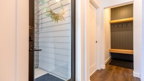 Un pasillo con puerta de vidrio, un banco de madera y un perchero.