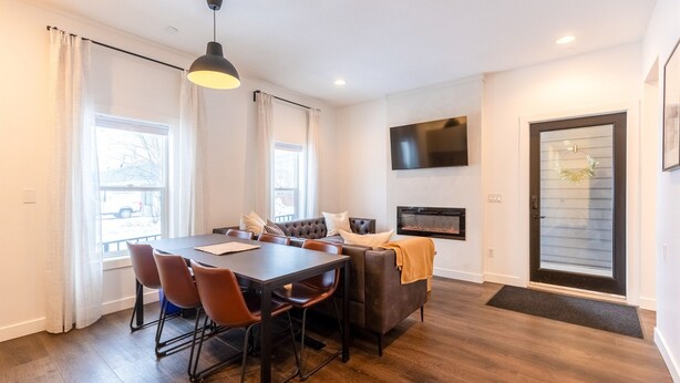 Un comedor moderno con una mesa y sillas de madera oscura, un sofá y un televisor montado en la pared.