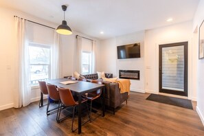 A modern dining area with a dark wood table and chairs, a sofa, and a TV mounted on the wall.