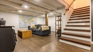 Una sala de estar moderna con suelo de madera, un sofá gris, una mesa de centro, un mapa mundial en la pared y una escalera con escalones de madera.
