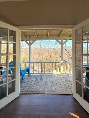 A covered porch with a wooden deck, a railing, and a view of leafless trees. - Stepping Stones Townhouse on Spring Street (Eureka Springs)