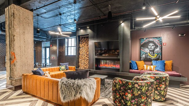 A modern lounge area with a fireplace, seating, and a large mural. - The Executive | 2BR | Rooftop Pool + Fireplace (St. Louis)
