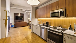A modern kitchen with wooden cabinets, a stainless steel microwave, a kettle, and a dishwasher. - The Executive | 2BR | Rooftop Pool + Fireplace (St. Louis)