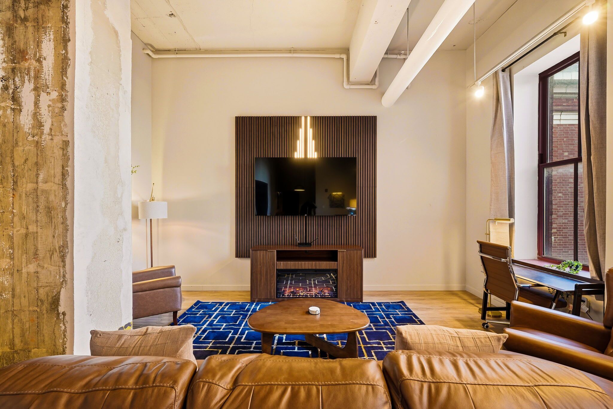 A modern living room with a fireplace, leather sofas, a coffee table, and a large TV screen.